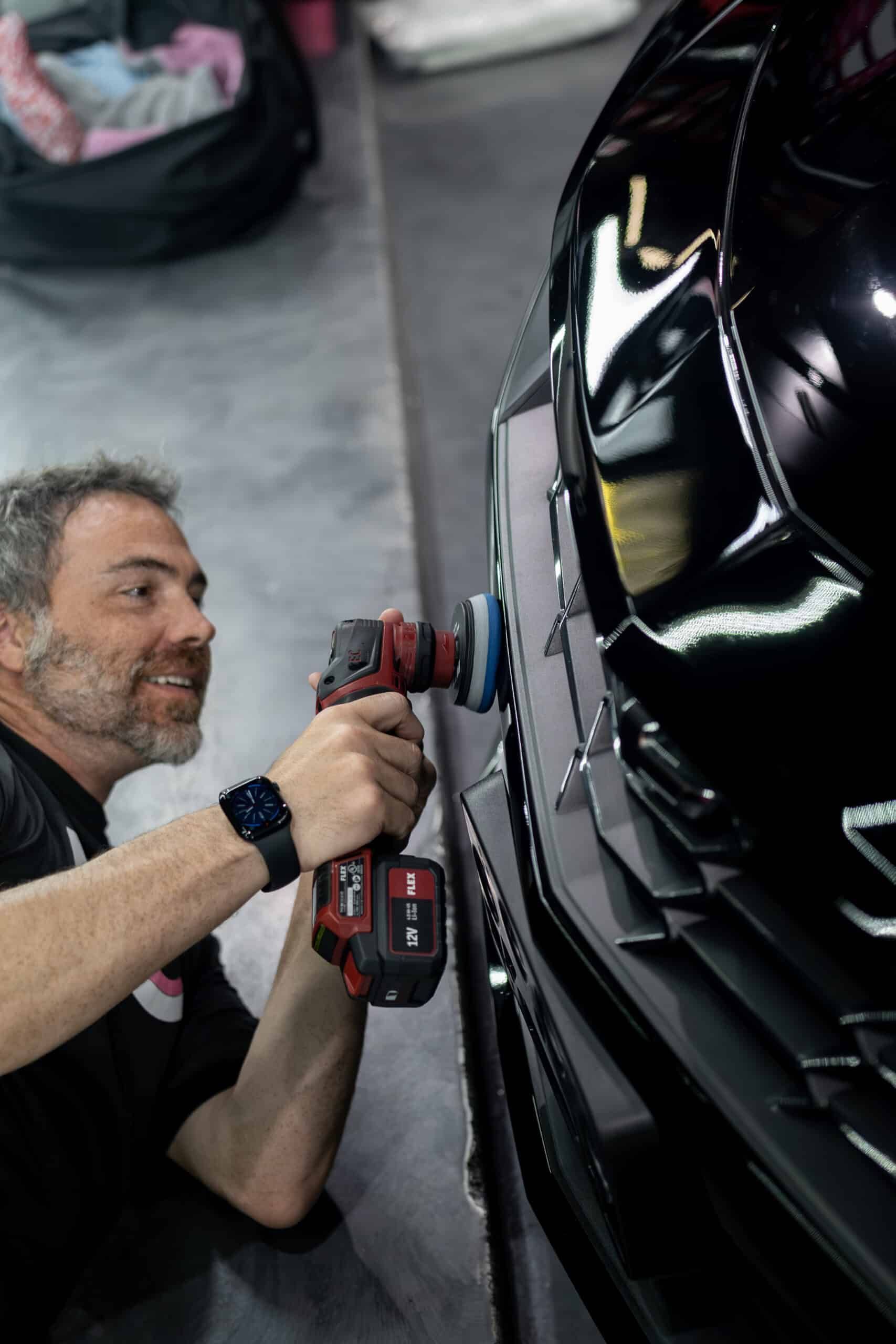 A man is polishing a black car with a drill.