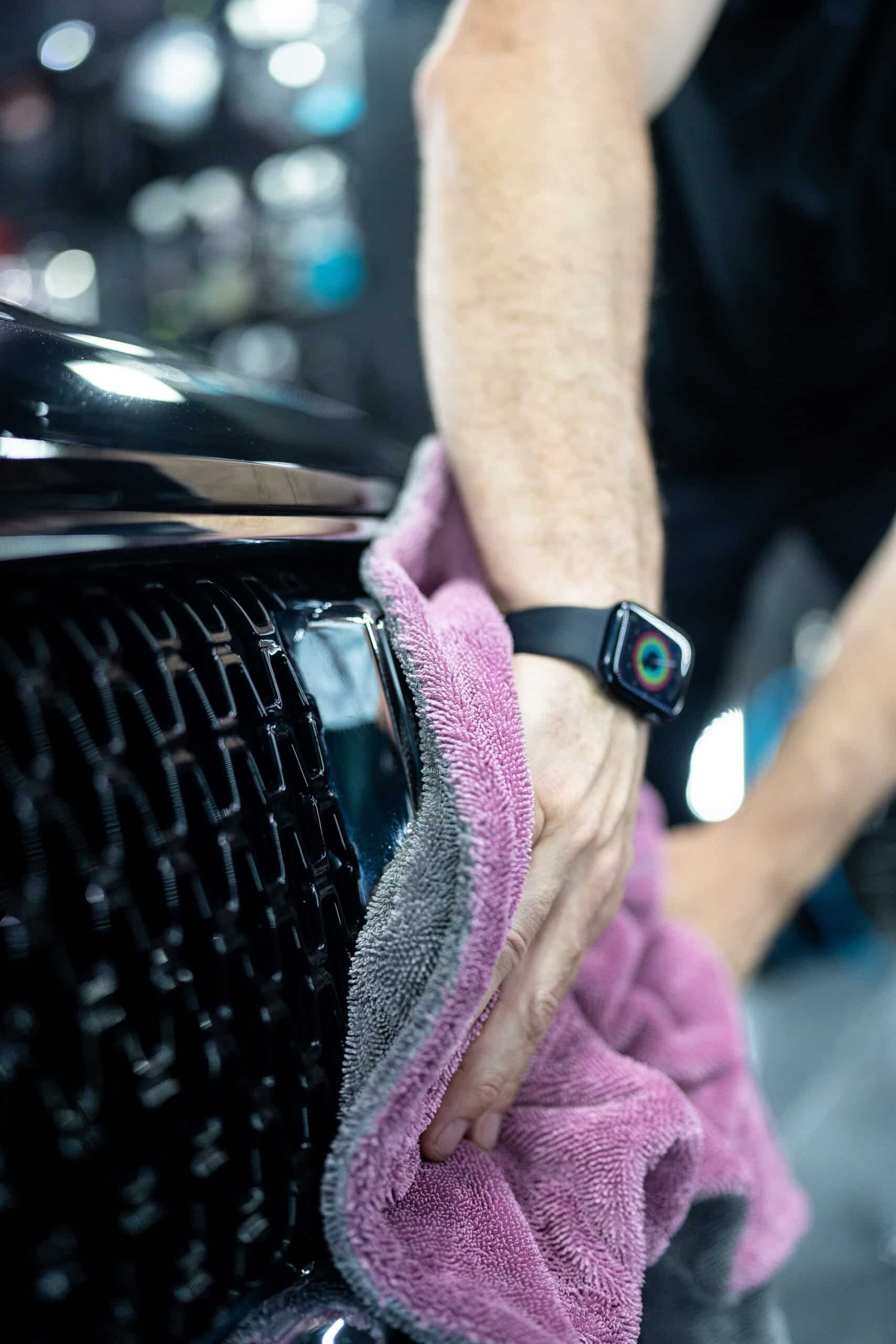 A man wearing an apple watch is cleaning a car with a towel.