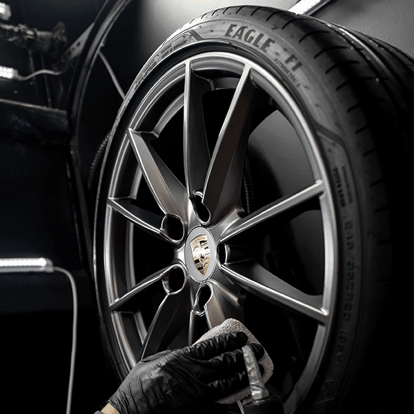 A person wearing black gloves is cleaning a car wheel with an eagle tire