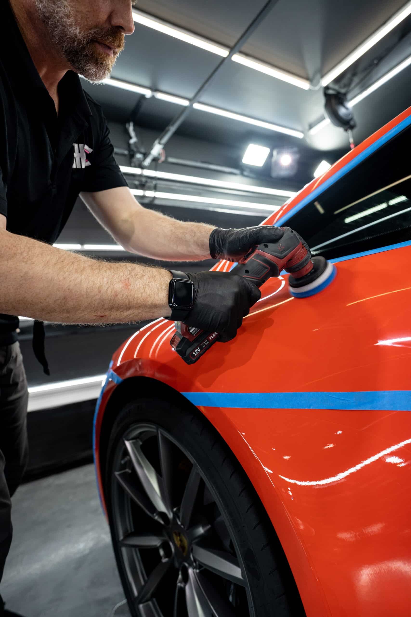 A man is polishing a red car in a garage.