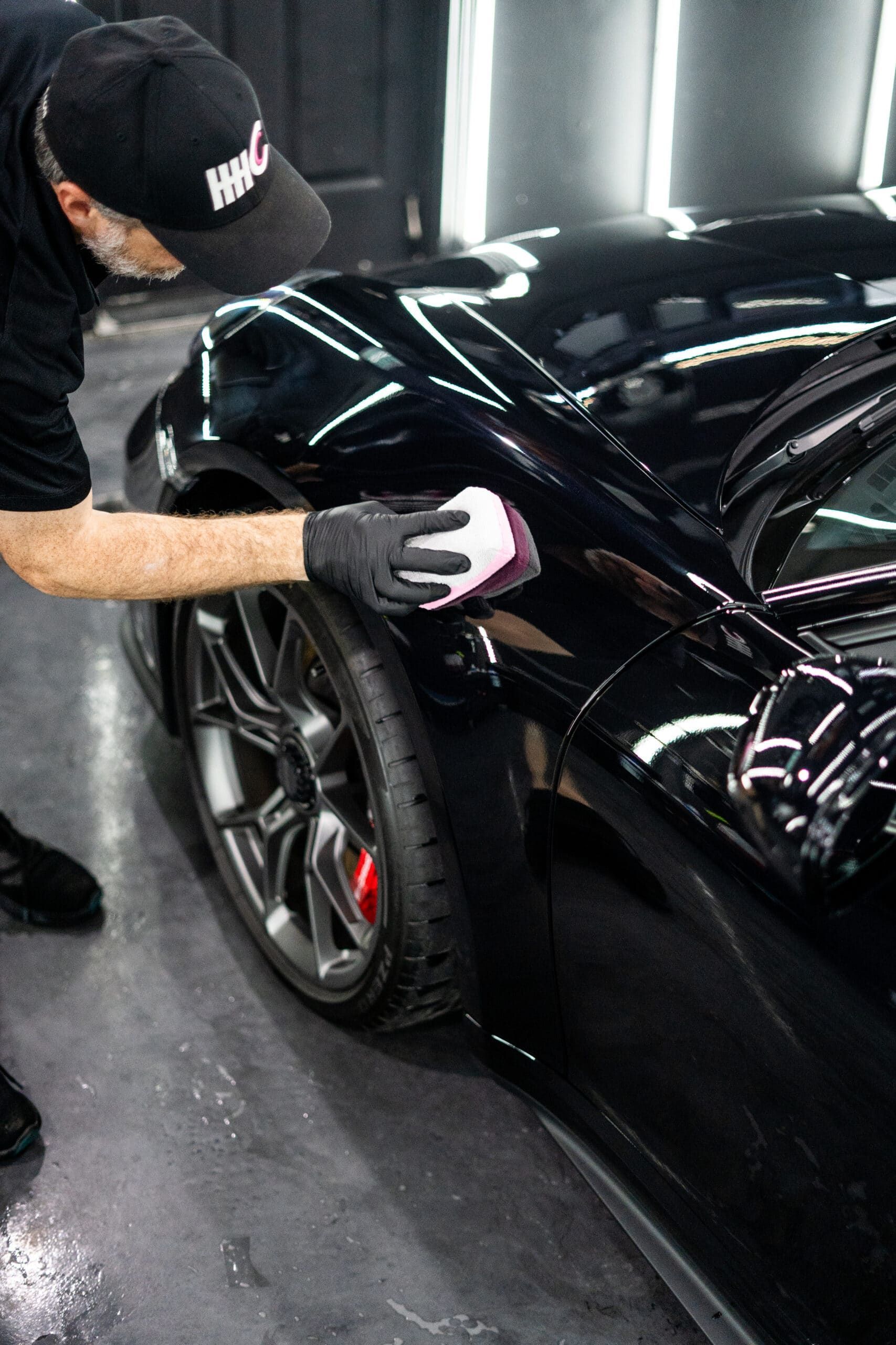 A man is polishing the fender of a black sports car.