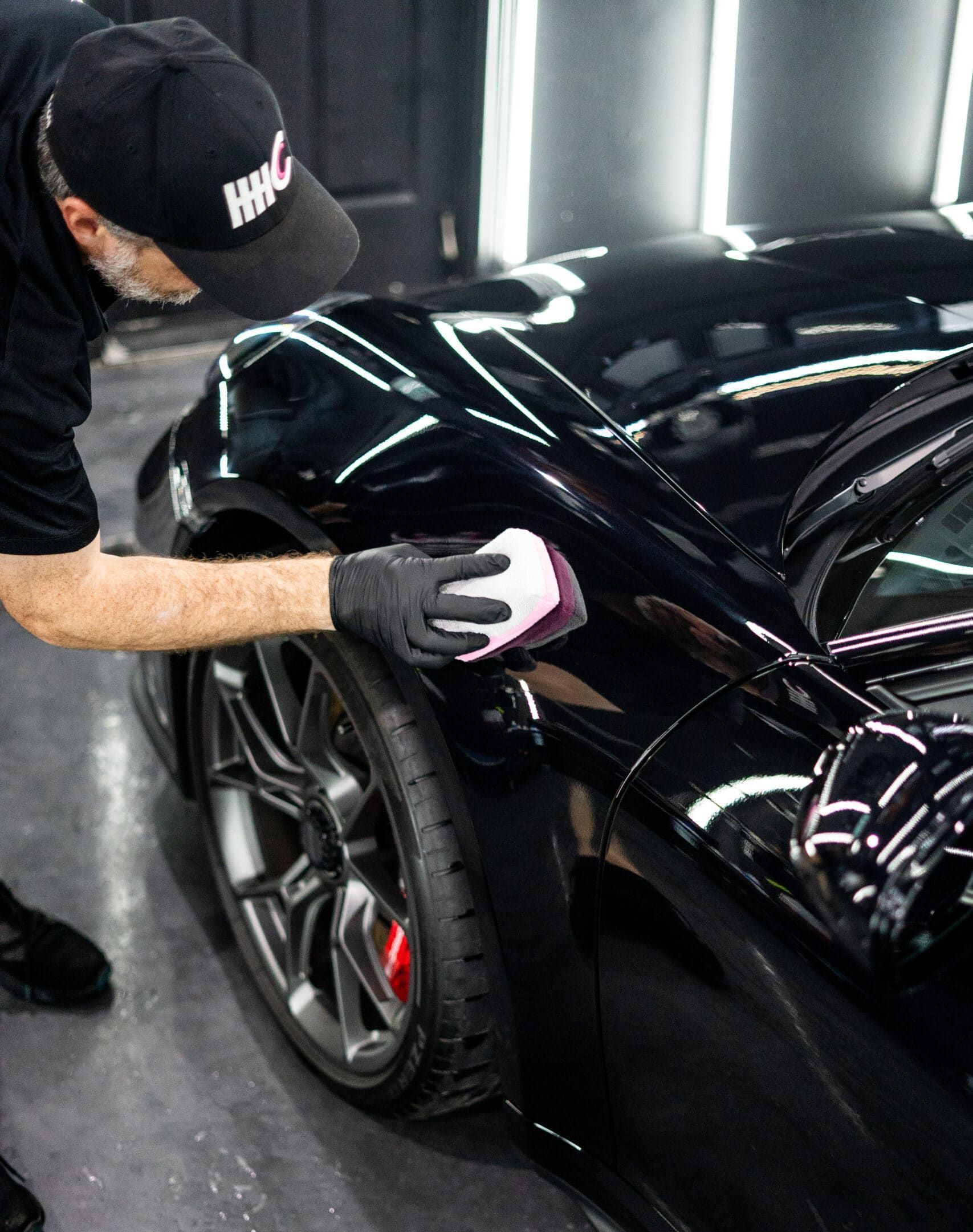 A man is polishing a black car with a sponge.