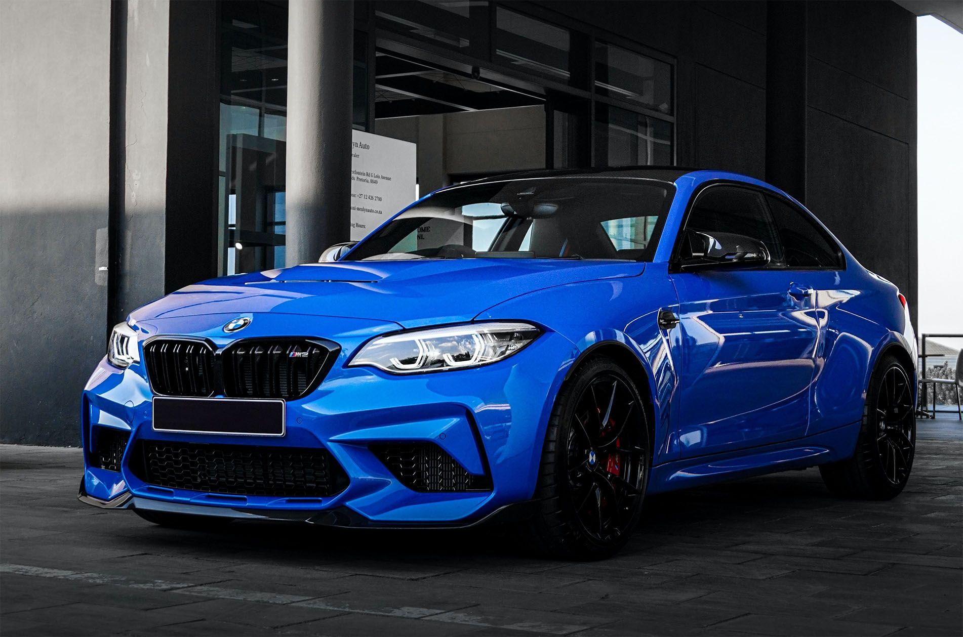 A blue bmw m2 is parked in front of a building.