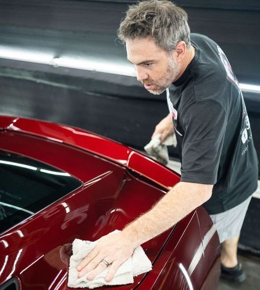 A man is cleaning a red car with a cloth