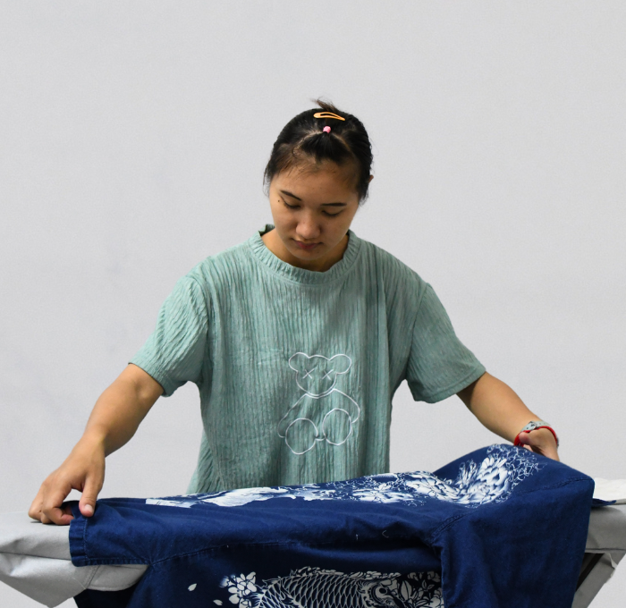 A woman is folding a blue shirt on an ironing board