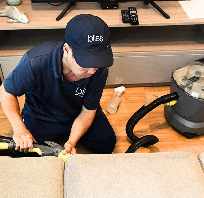 A man wearing a bliss hat is cleaning a couch