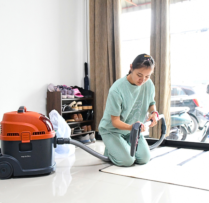 A woman is kneeling on the floor using a vacuum cleaner