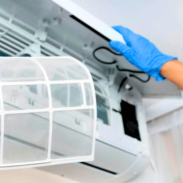 A person wearing blue gloves is cleaning an air conditioner.