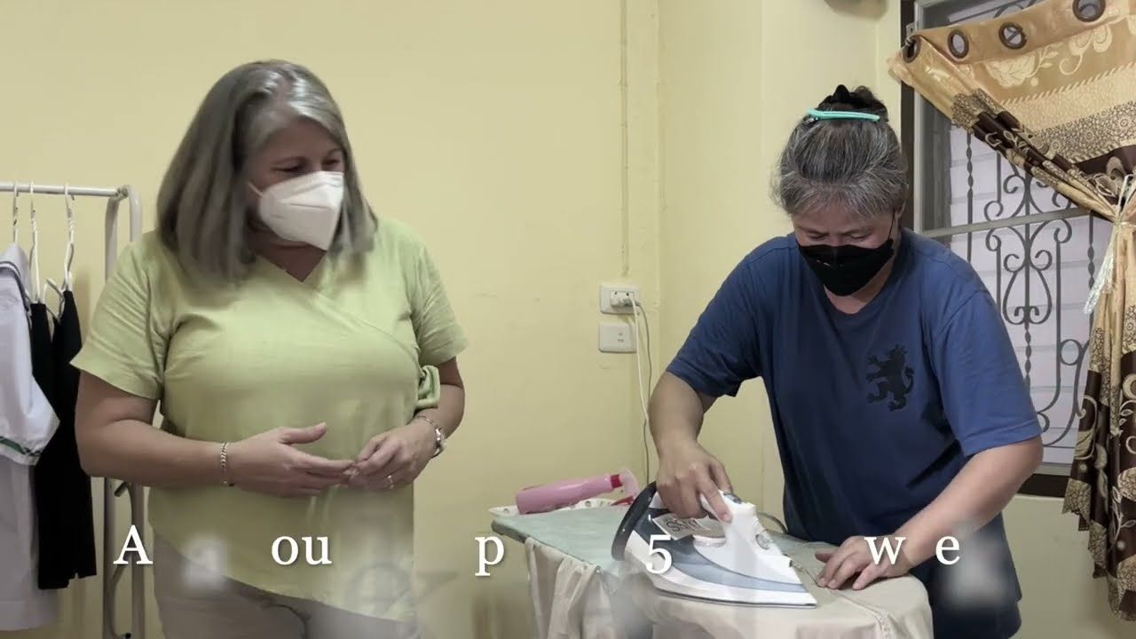 Two women wearing masks are ironing clothes in a room.