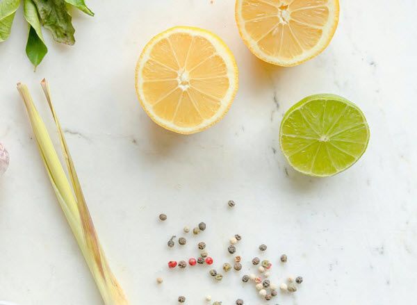 A cutting board topped with lemons , limes , peppercorns and lemongrass.