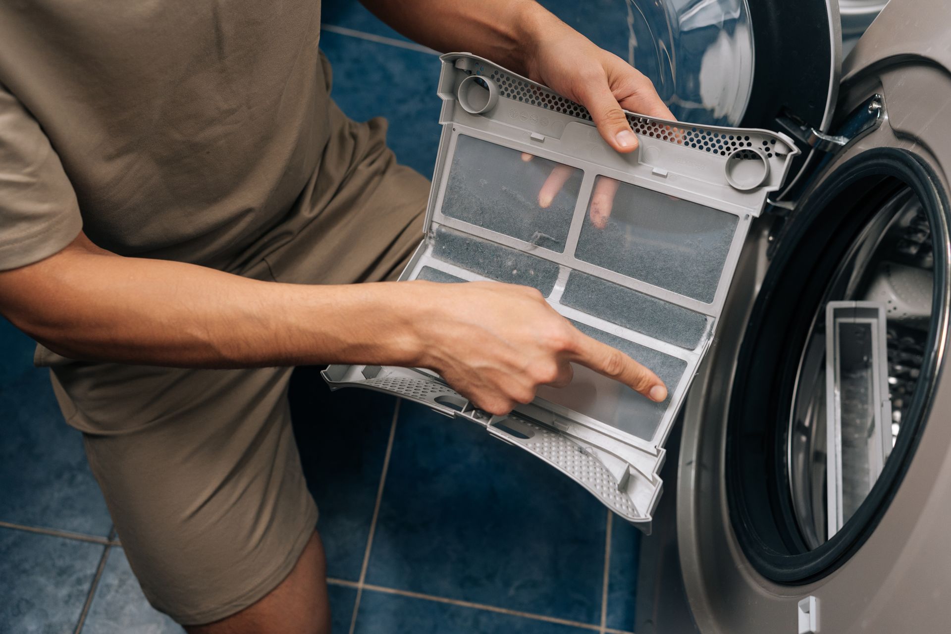 Person cleaning a washing machine filter, pointing to lint buildup inside the appliance Person cleaning a washing machine filter, pointing to lint buildup inside the appliance