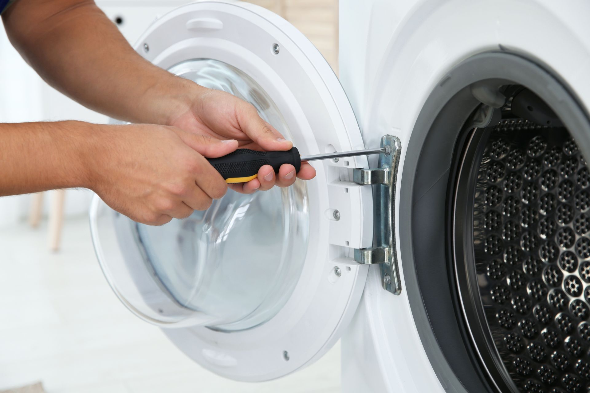 Hands using a screwdriver to repair the hinge of a front-loading washing machine. Hands using a screwdriver to repair the hinge of a front-loading washing machine.