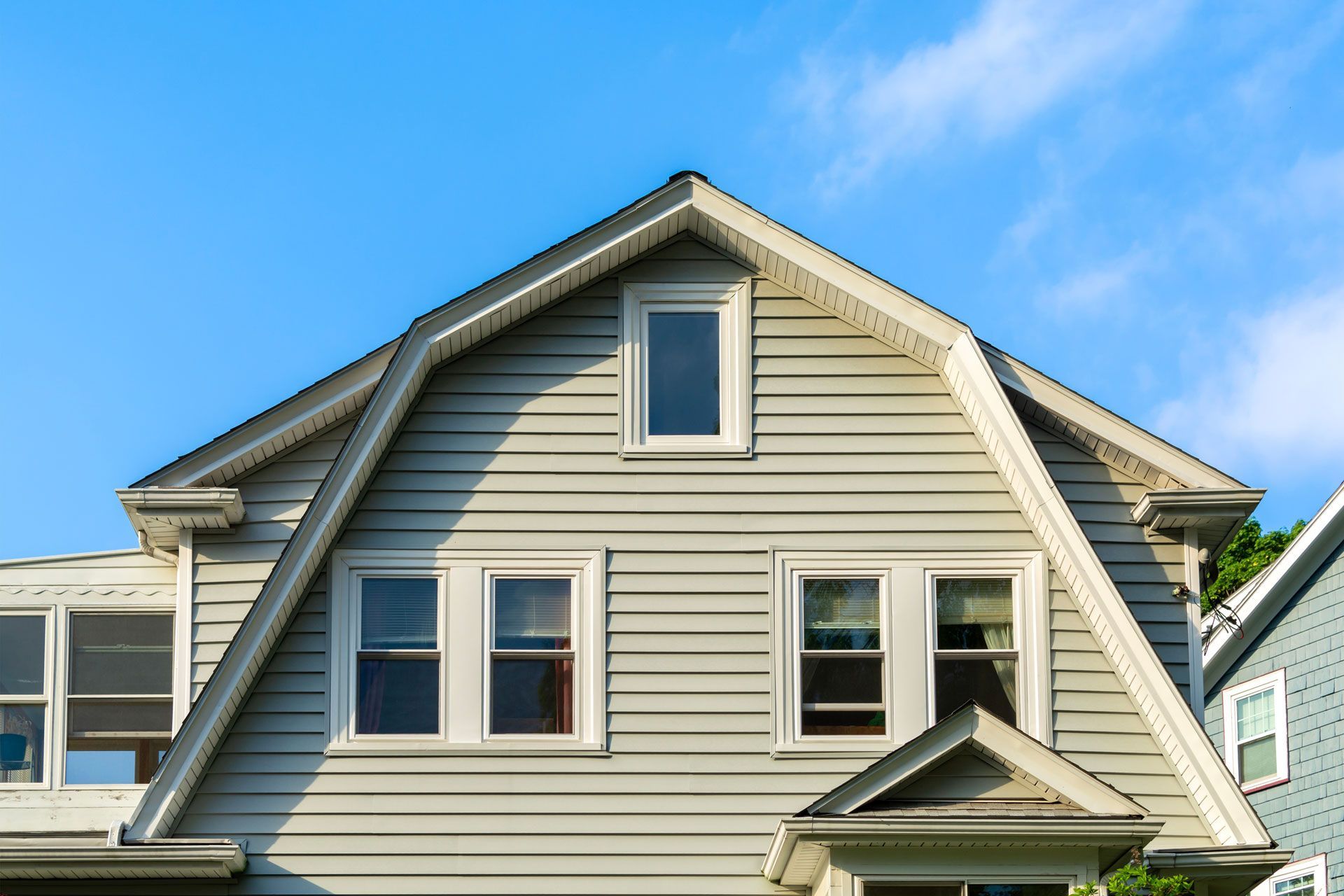 Gray house with triangular dormer, small window, blue sky.