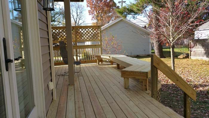 Wooden deck with built-in bench, leading to a yard with a small building and fall foliage.