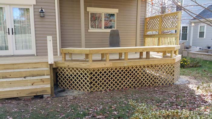 Wooden deck with lattice skirting and railing, next to a house with glass doors.