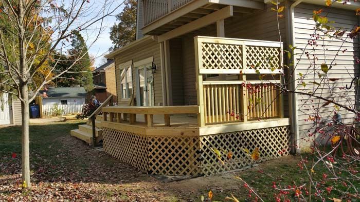 Wooden deck with lattice detailing, connected to a light beige building with a door and windows.