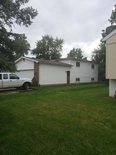 White two-story house with green lawn, pickup truck, cloudy sky.
