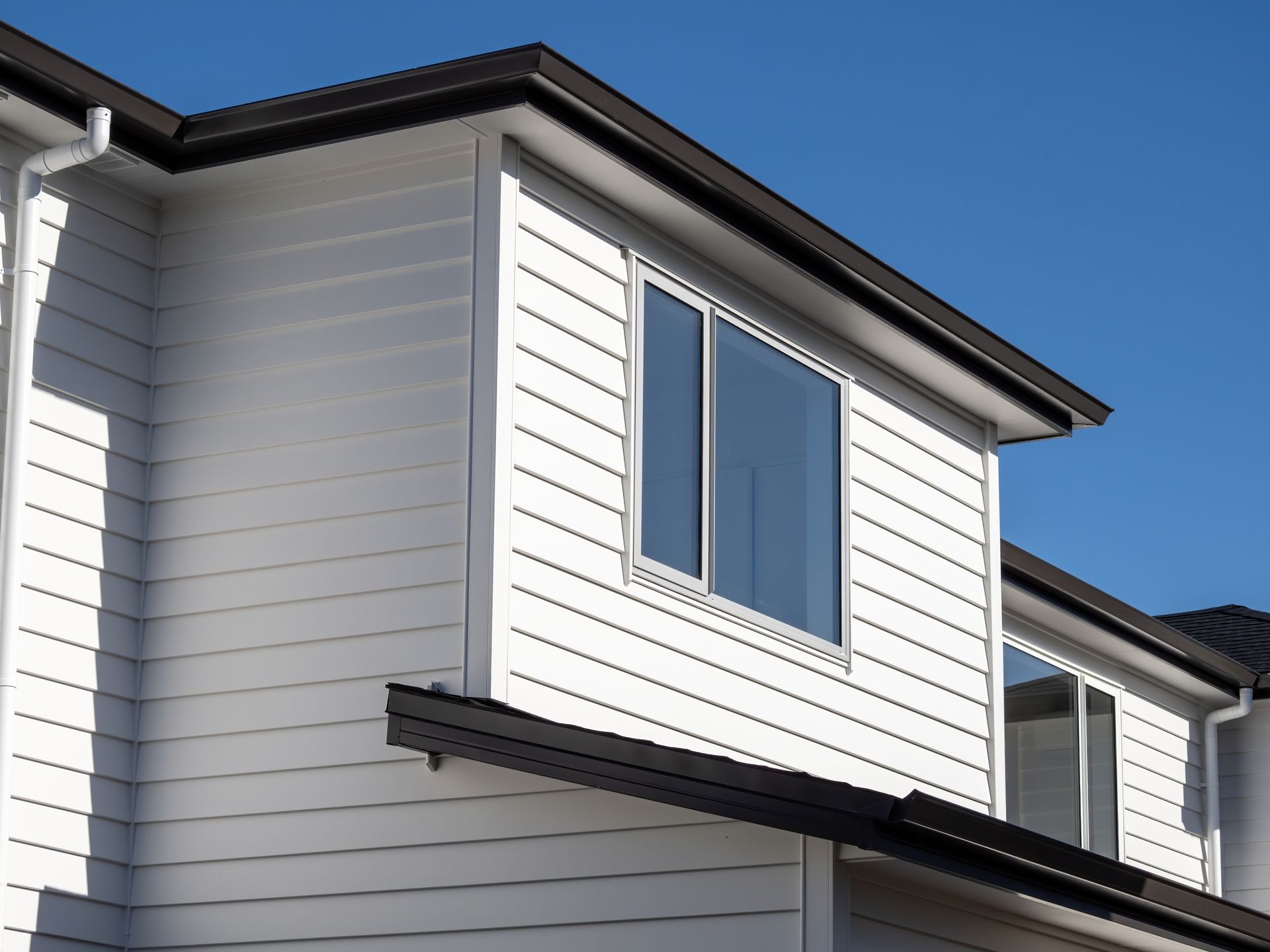 White house with horizontal siding and black roof against a blue sky.
