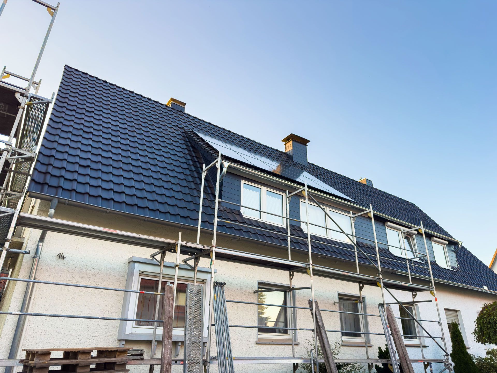House with new dark gray roof and scaffolding during construction, against a clear blue sky.