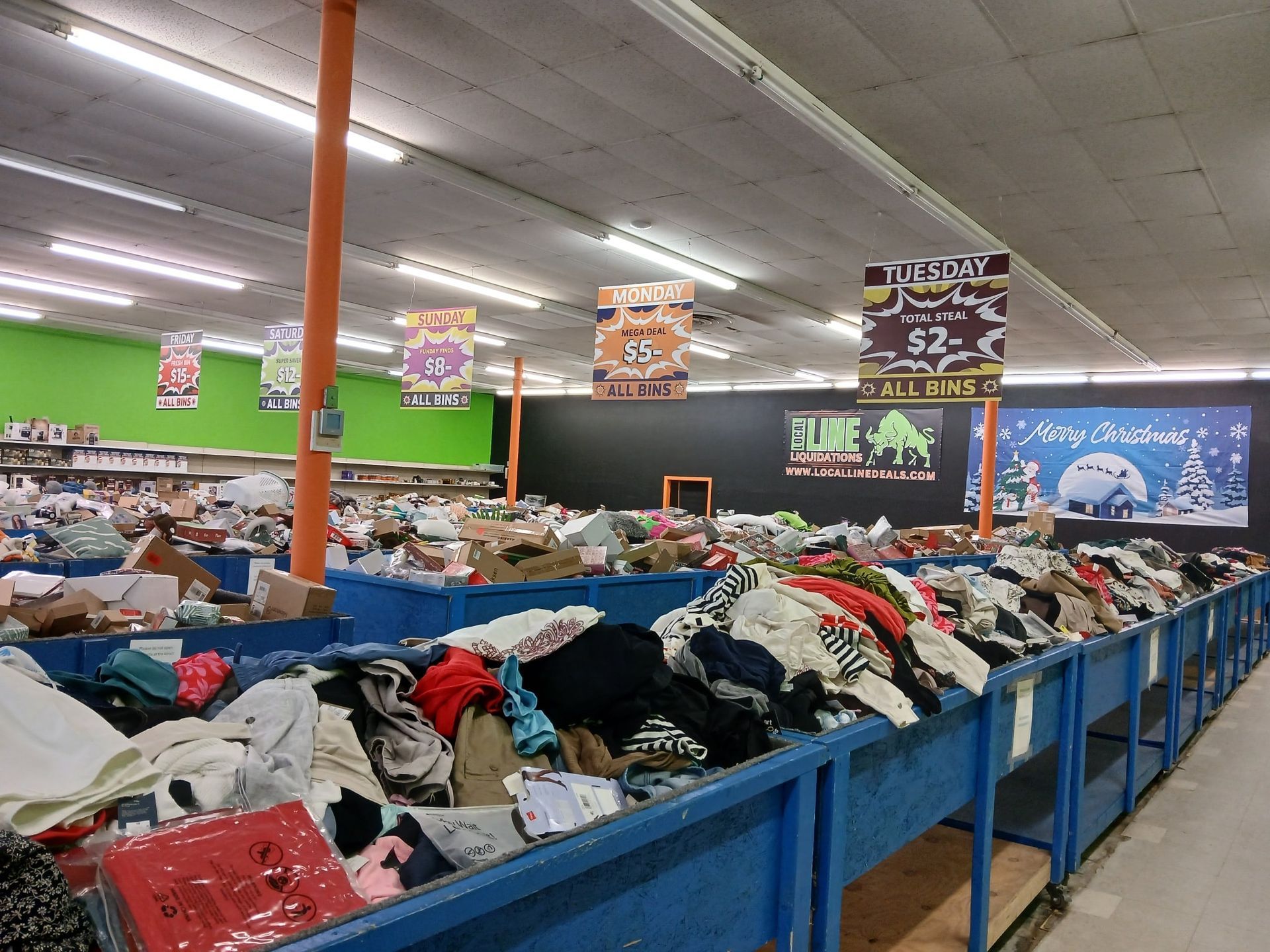 Inside a discount store: Clothing bins filled, signs overhead, brightly lit, large open space.