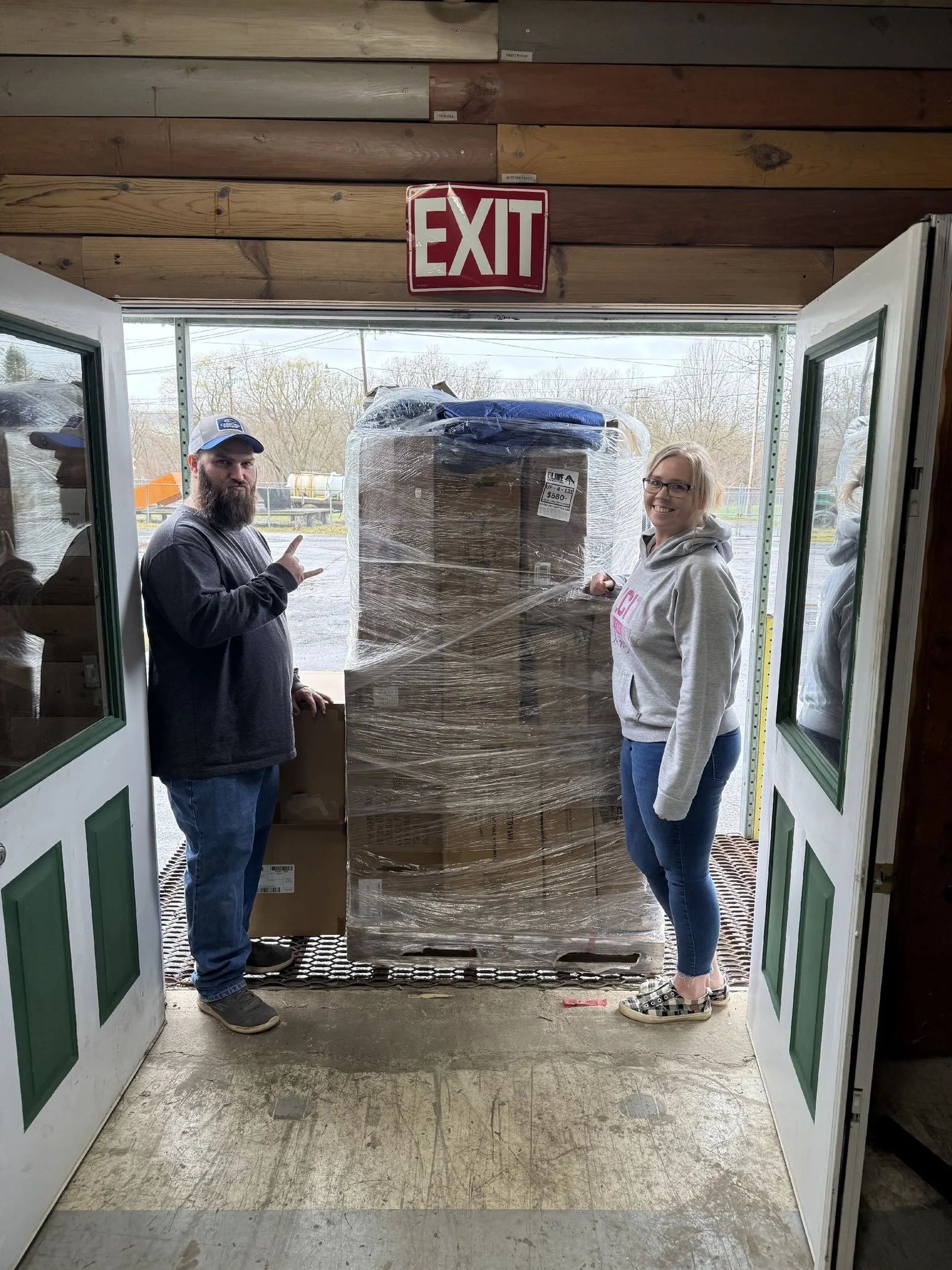A man and a woman are standing in front of a large stack of boxes.