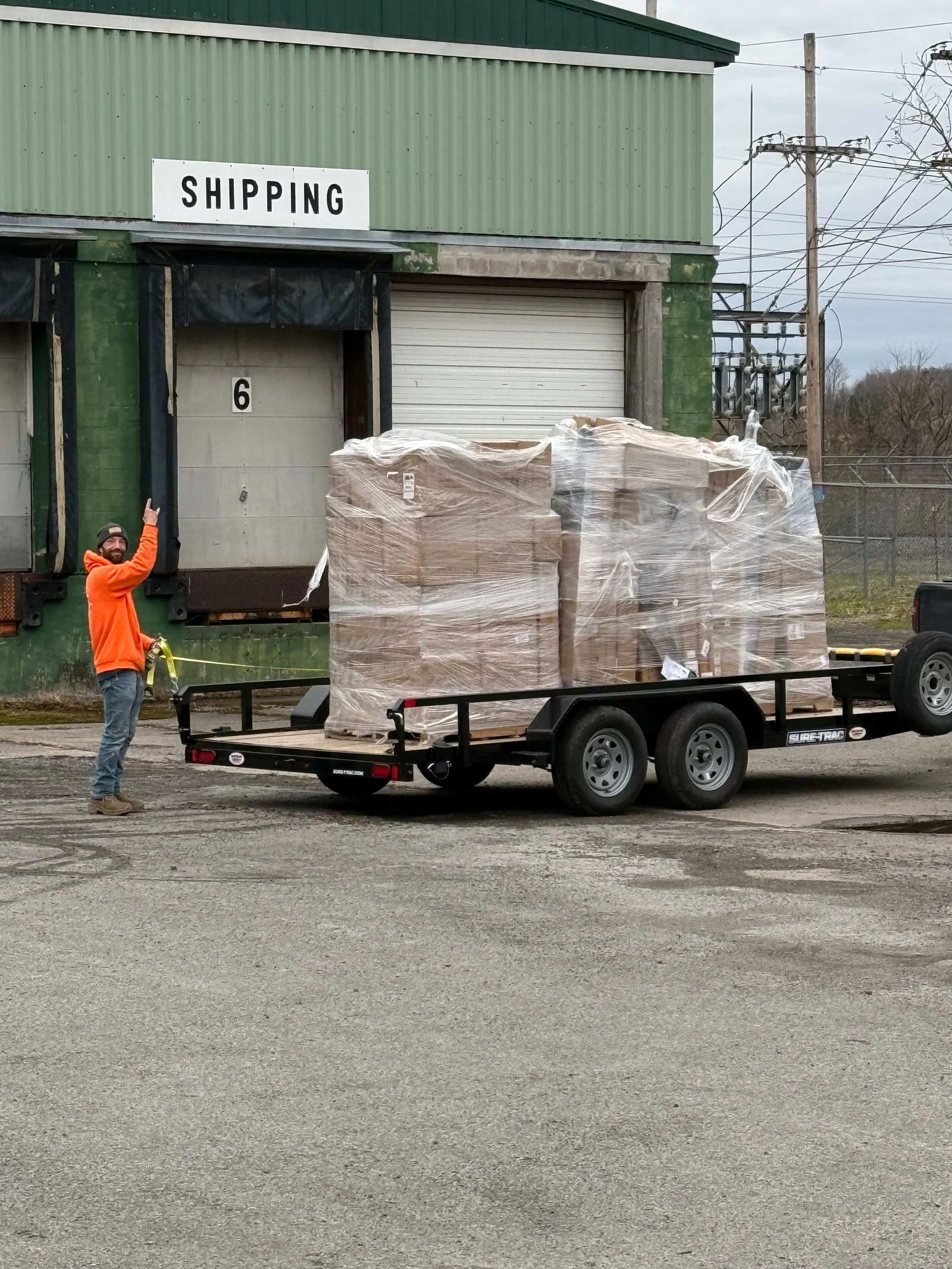 A man is standing next to a trailer with a large stack of boxes on it.