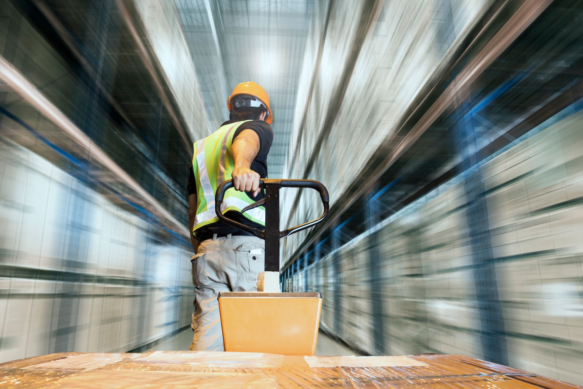 A man is pushing a pallet truck in a warehouse.