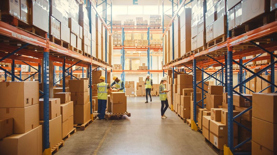 A group of people are working in a large warehouse filled with lots of boxes.