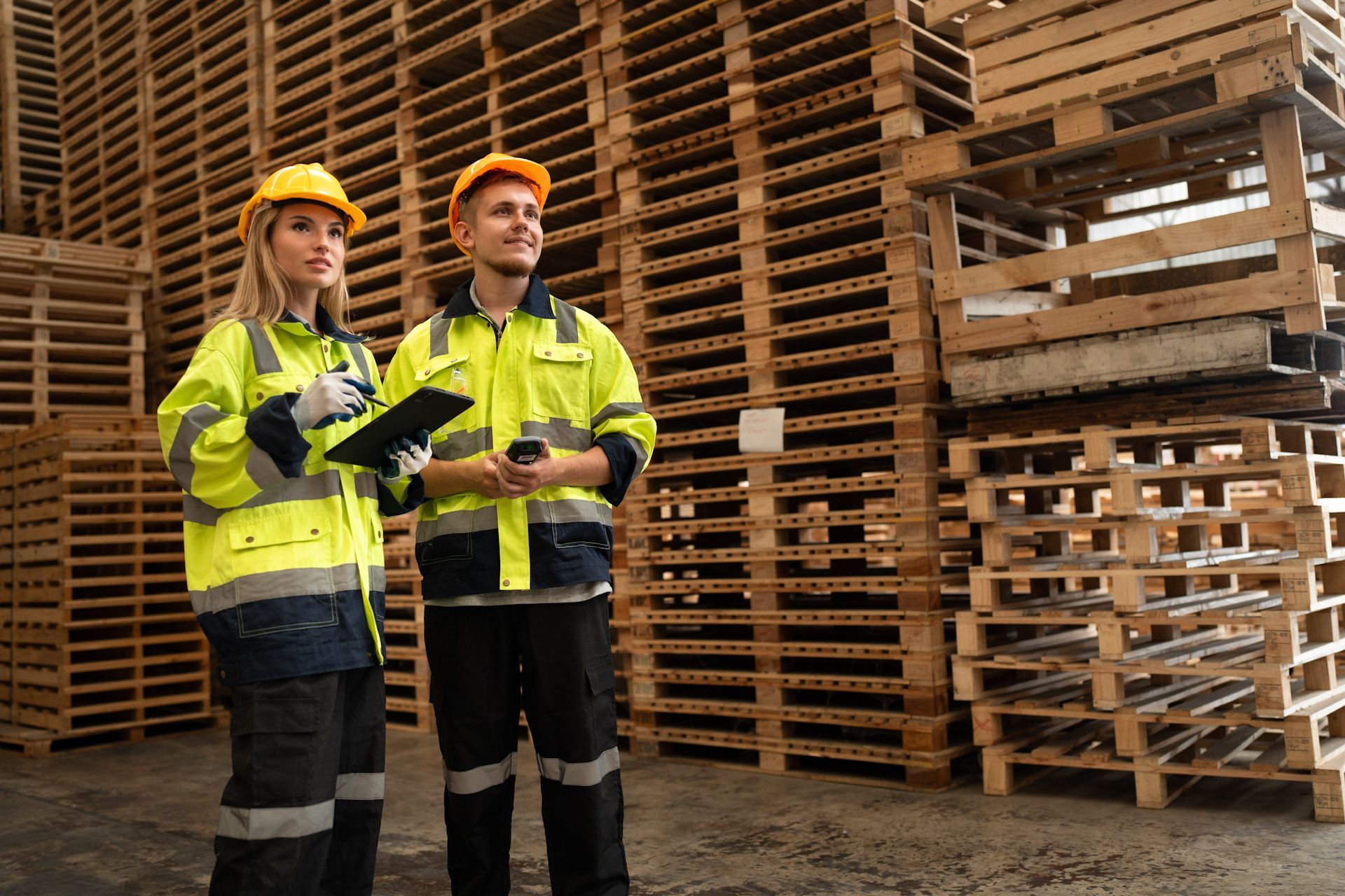 A man and a woman are standing in front of a stack of wooden pallets.