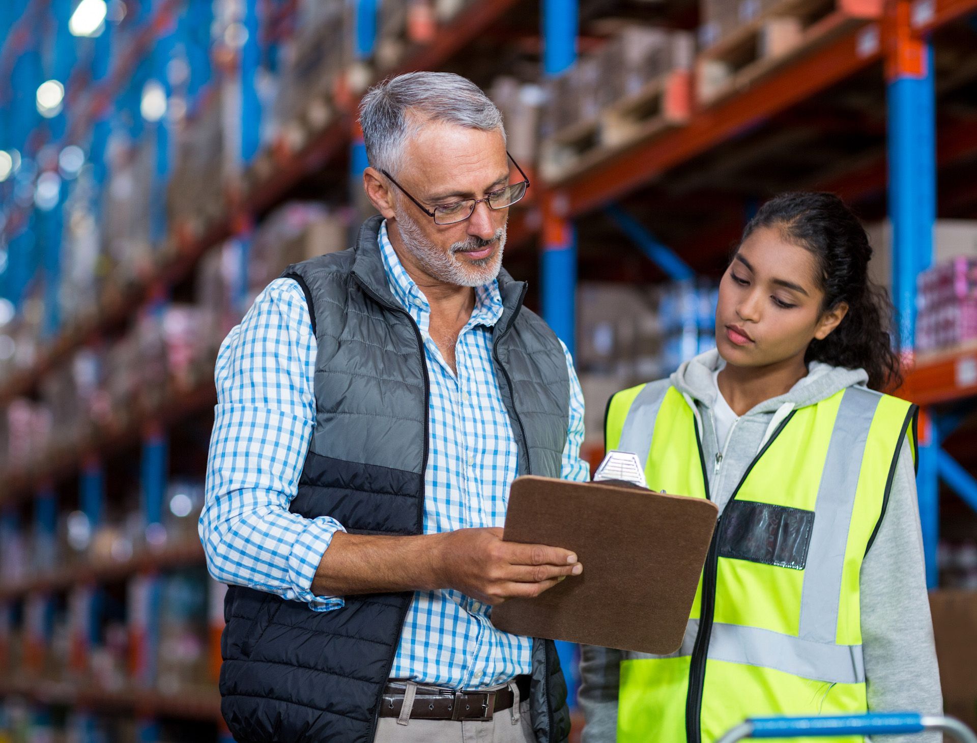 A man and a woman are looking at a clipboard in a warehouse.