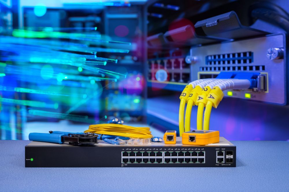 Server room with network switch and cables. Bright blue fiber optic lines, yellow and blue cords.