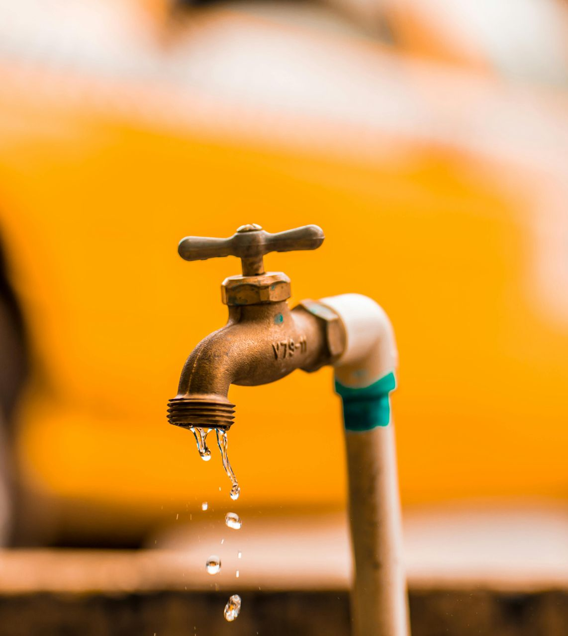 Water dripping from a bronze faucet against an orange background.