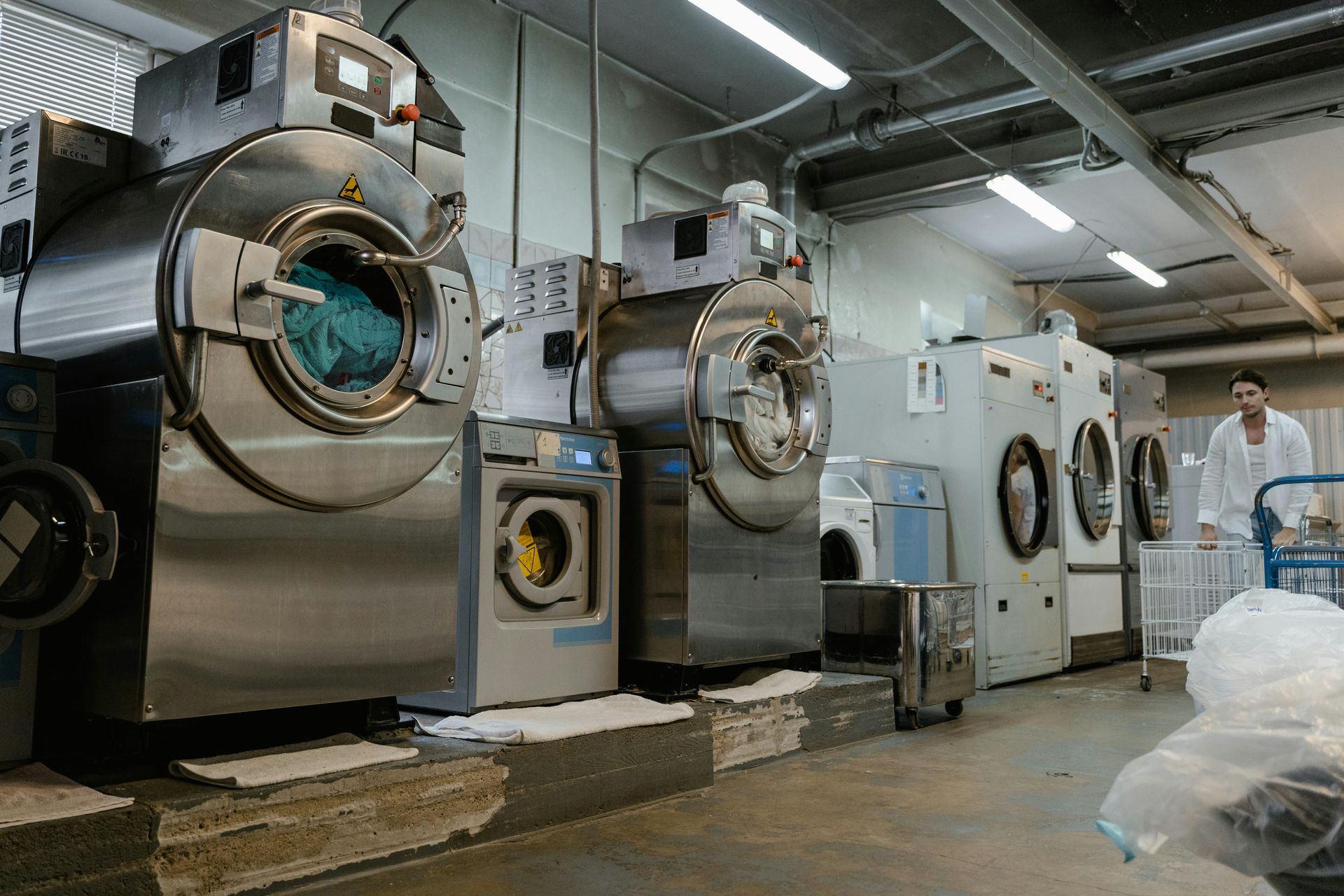Laundry facility with multiple industrial washing machines, and a worker pushing a cart.