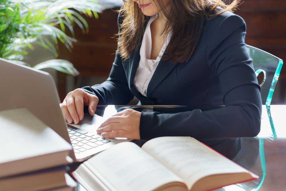 Woman in Suit Working on A Laptop, Open Book, in An Office Setting — Bespoke Legal Group In Southport, QLD