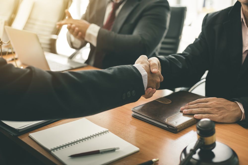 Two Men in Suits Shaking Hands at A Table, Possibly After a Deal — Bespoke Legal Group In Northern, NSW