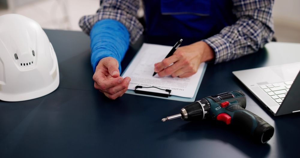Person with arm in cast writing on clipboard near a hard hat, laptop, and drill — Bespoke Legal Group In Southport, QLD