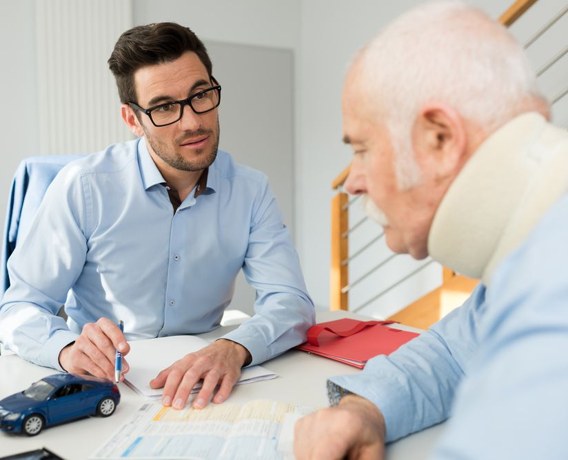 Man in glasses reviews documents with a man wearing a neck brace. A toy car sits on the table — Bespoke Legal Group In Southport, QLD