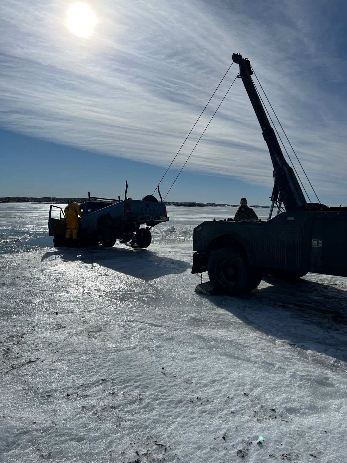A truck towing a vehicle on a bright, icy surface under a sunny sky.