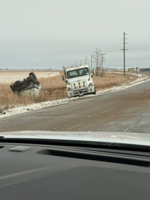 White semi-truck off road in snowy ditch next to a damaged object; overcast day on a rural road.