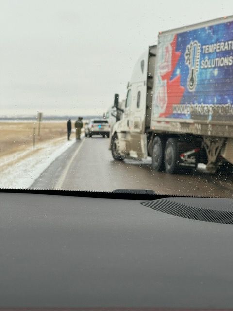 Semi-truck on a road with emergency vehicles and people standing nearby on a cloudy day.