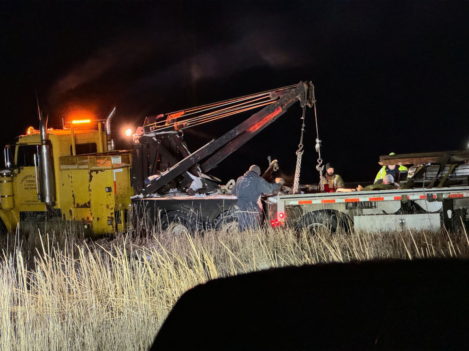 Yellow tow truck at night, loading onto a flatbed trailer in a field.