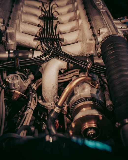 Close-up view of a car engine's intricate components, including wires, pipes, and metallic parts, in a dimly lit setting.