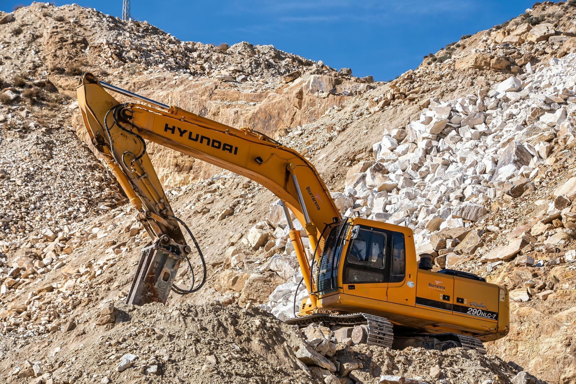 Yellow Hyundai excavator digging in a rocky quarry under a blue sky