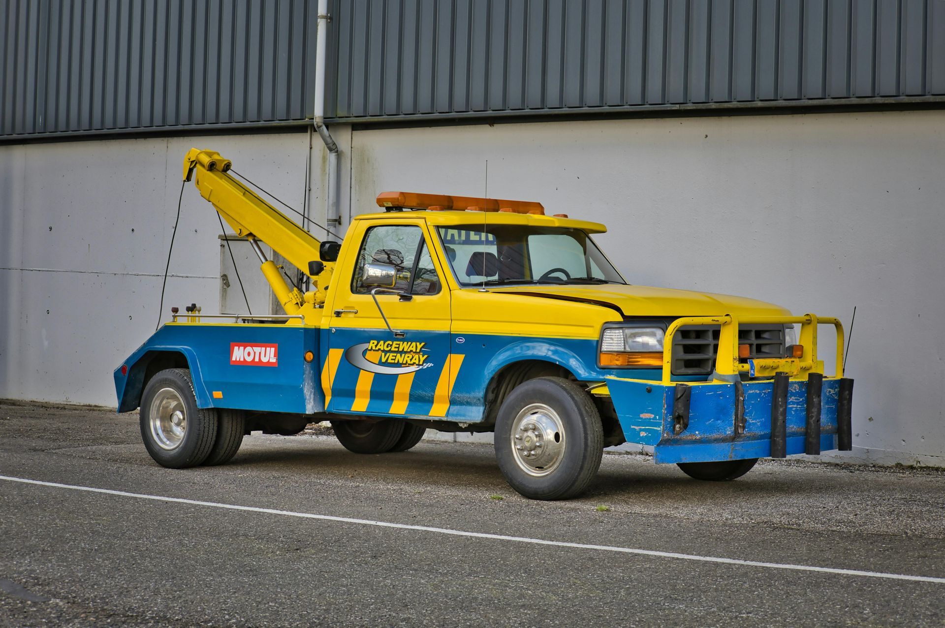 Yellow and blue tow truck parked next to a gray building.