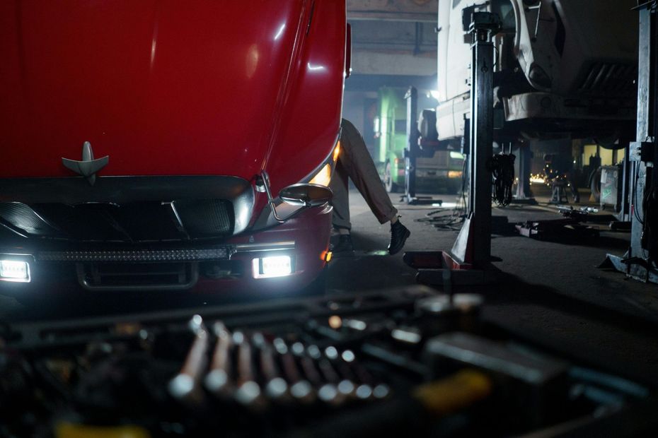 Mechanic working under a red truck in a garage. Tool kit in the foreground.