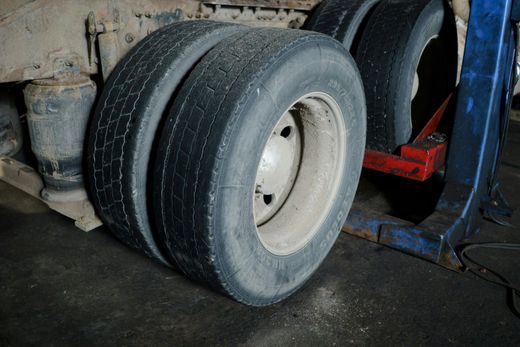 Dual truck tires, weathered, mounted on a rim, viewed close up in an indoor garage setting.