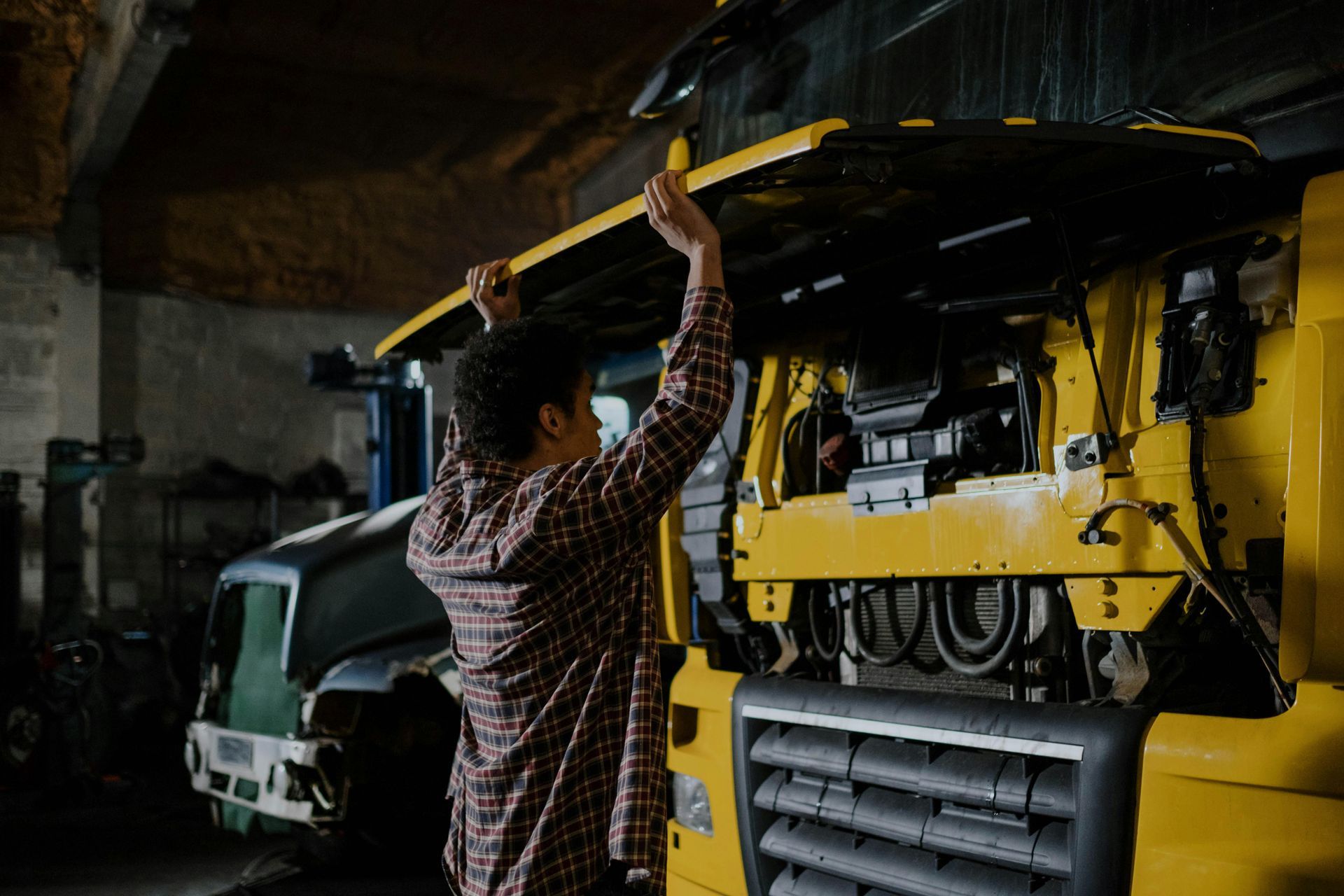 Person lifts hood of large yellow vehicle in a garage.