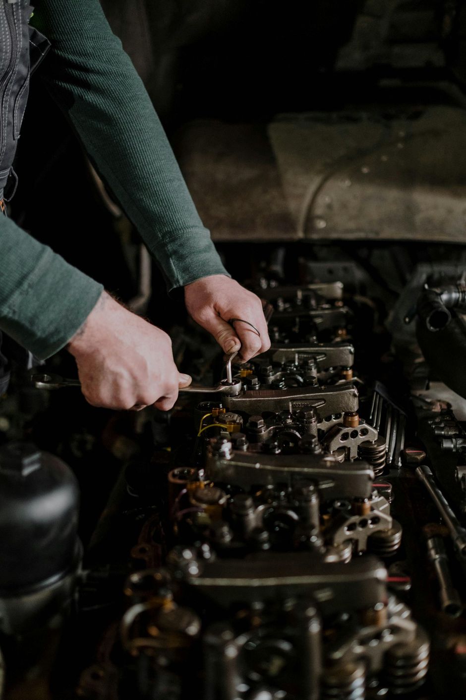 Mechanic working on an engine with a wrench, in a dimly lit garage.