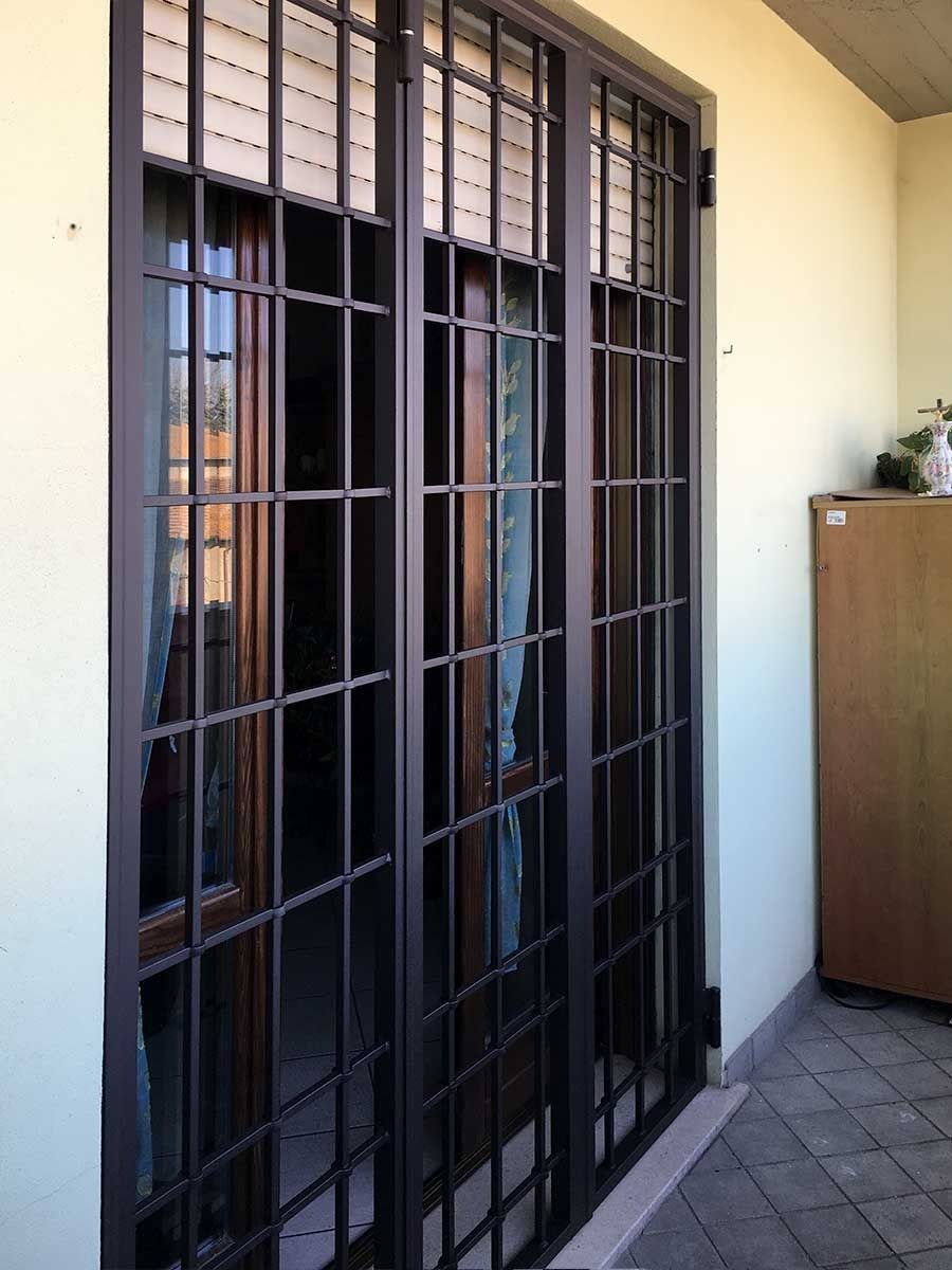 Sbarre di sicurezza in metallo nero sopra una porta a vetri su un patio piastrellato accanto a un muro color crema