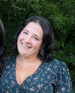 A woman with gray hair is smiling and wearing a black shirt and necklace.